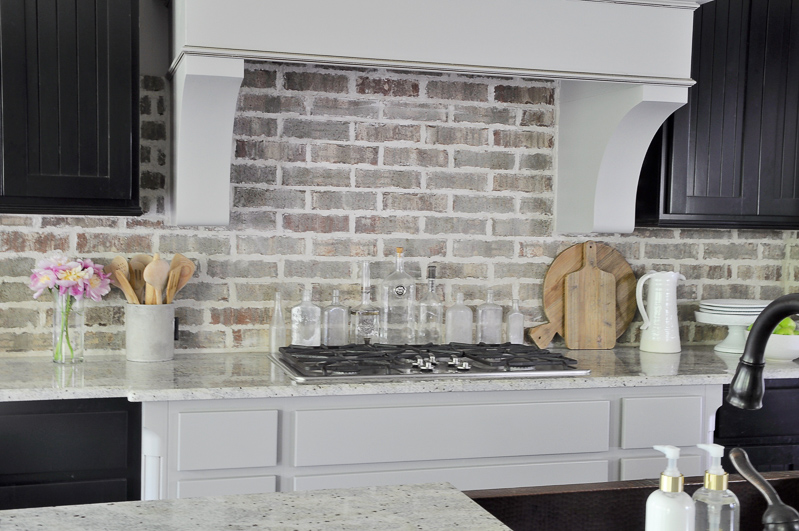 Gorgeous kitchen with brick backsplash large vent hood and black cabinets