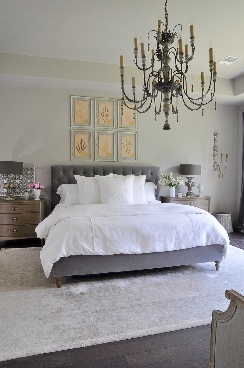 white and gray master bedroom with large chandelier and botan