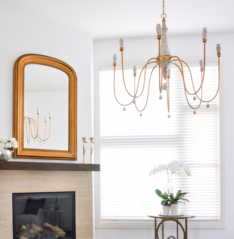 elegant arched gold mirror and chandelier over fireplace